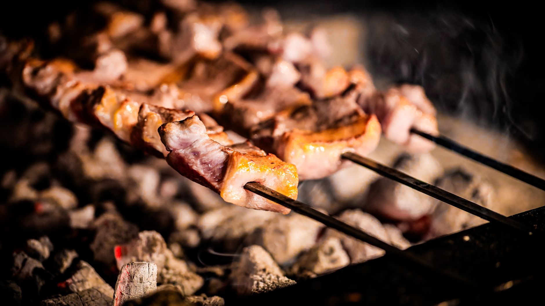Skewers of marinated lamb cooking over a charcoal grill, fat catching the flame