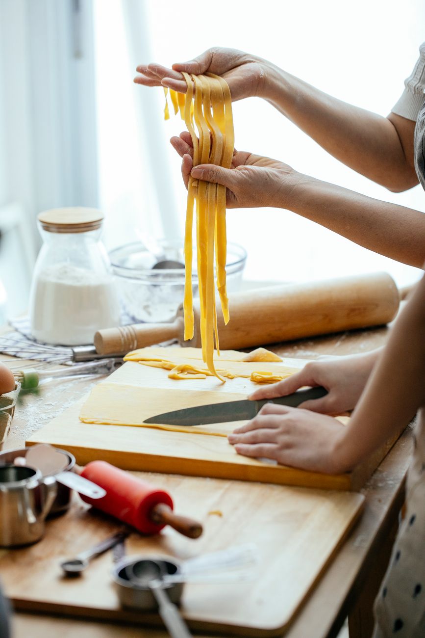 A cook's floured hands rolling and cutting fresh pasta on a wooden bench in the Italian side of the kitchen